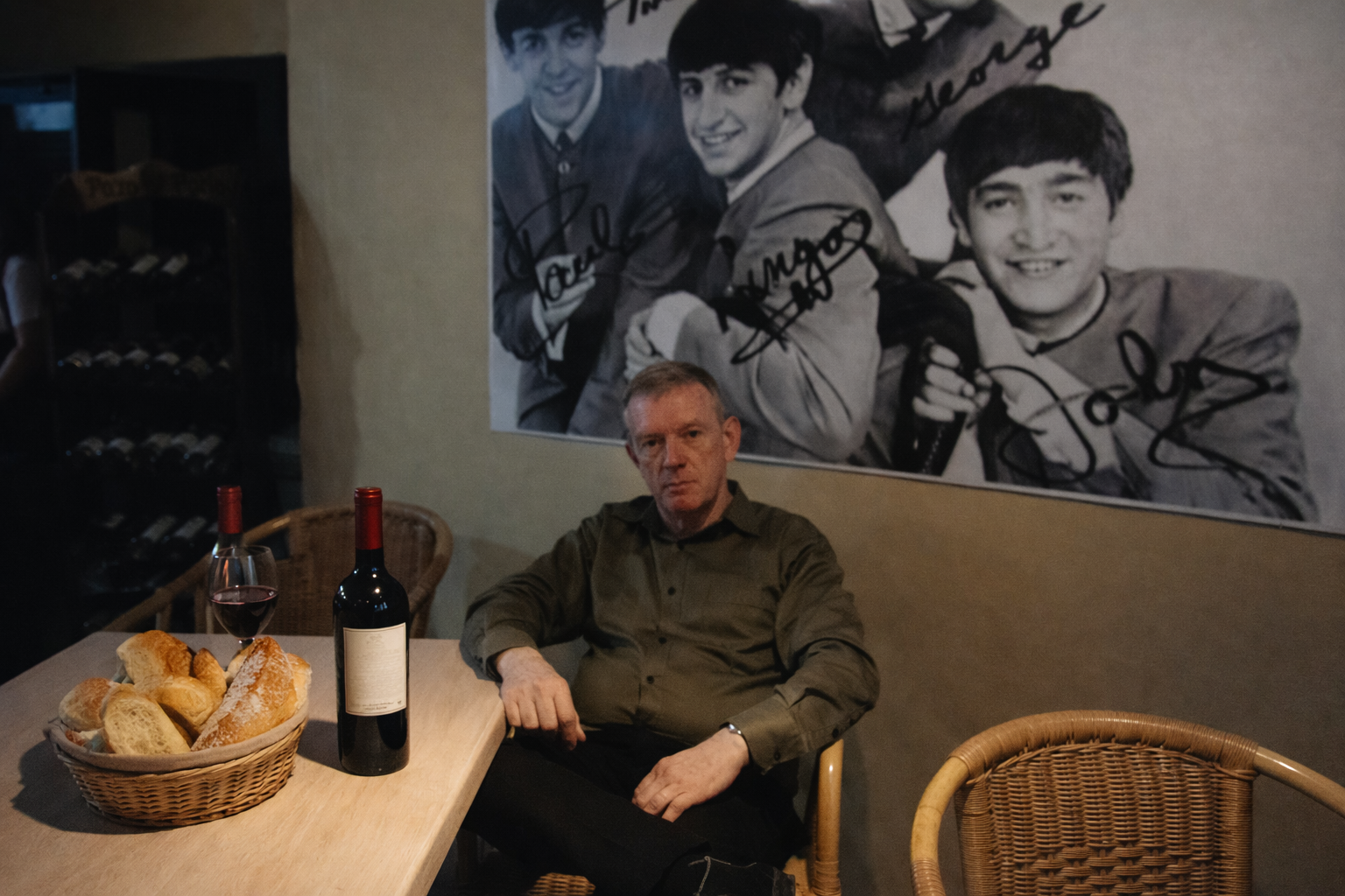 Orlando L. Rodríguez González ante una mesa con pan y vino tinto, a su espalda afiche de los Beatles